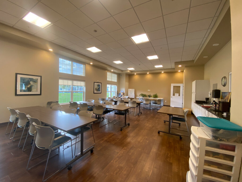 Long activity room set up with tables and chairs at Traditions of Saginaw with art and crafts in bins.