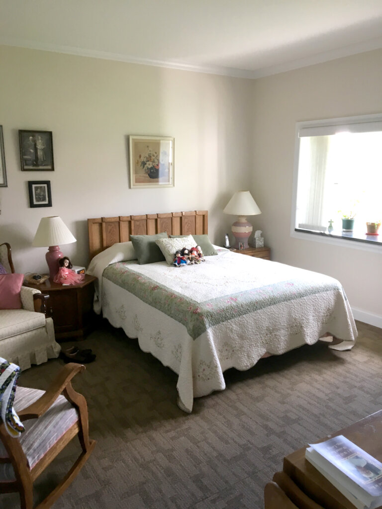 Picture of a bedroom. Tan walls with picture frames and brown patterned carpet. White and green bedding.