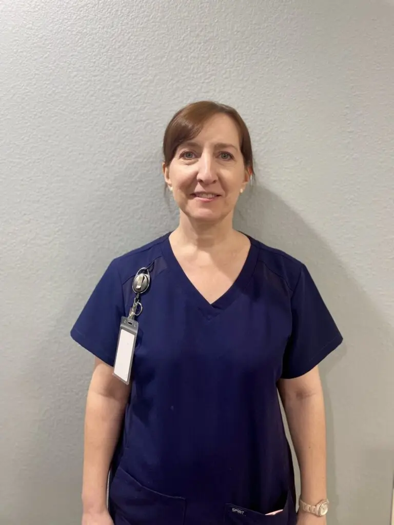 A female nurse with her hair tied back in a ponytail wearing dark blue scrubs