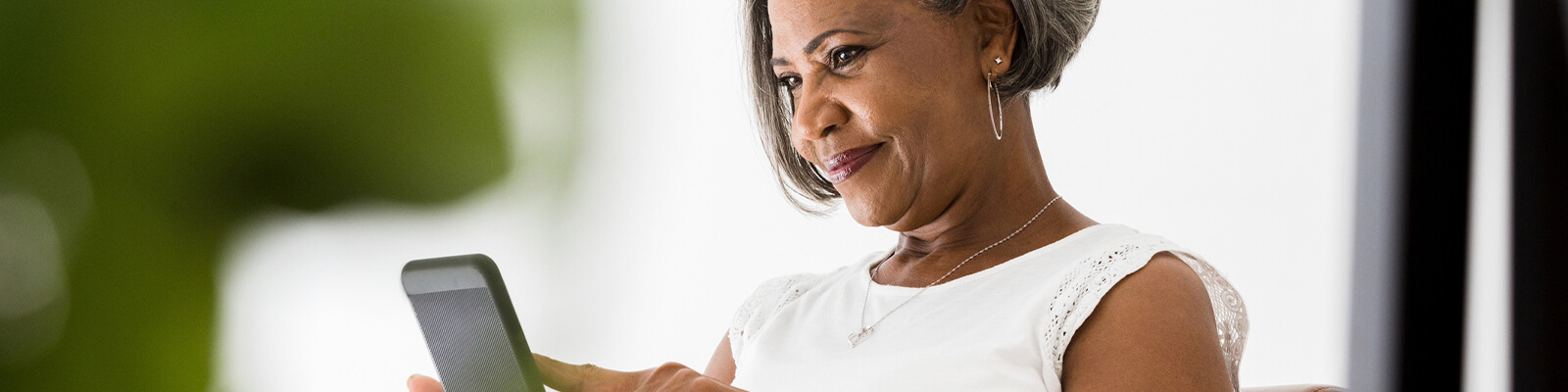 Senior woman wearing a white shirt smiling looking down at smartphone