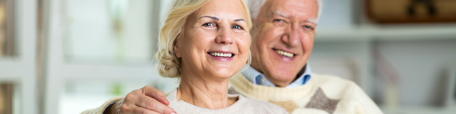 A senior couple sitting together smiling as the man put's his arm around the woman's shoulder