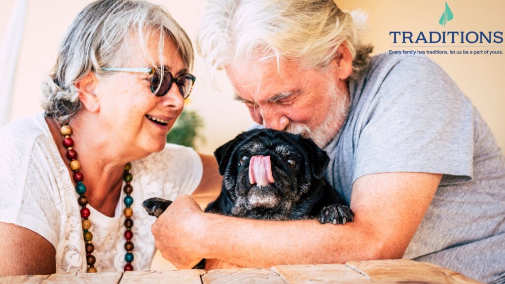 Senior man and senior woman at Traditions of Saginaw hugging their pet pug while sitting in their apartment