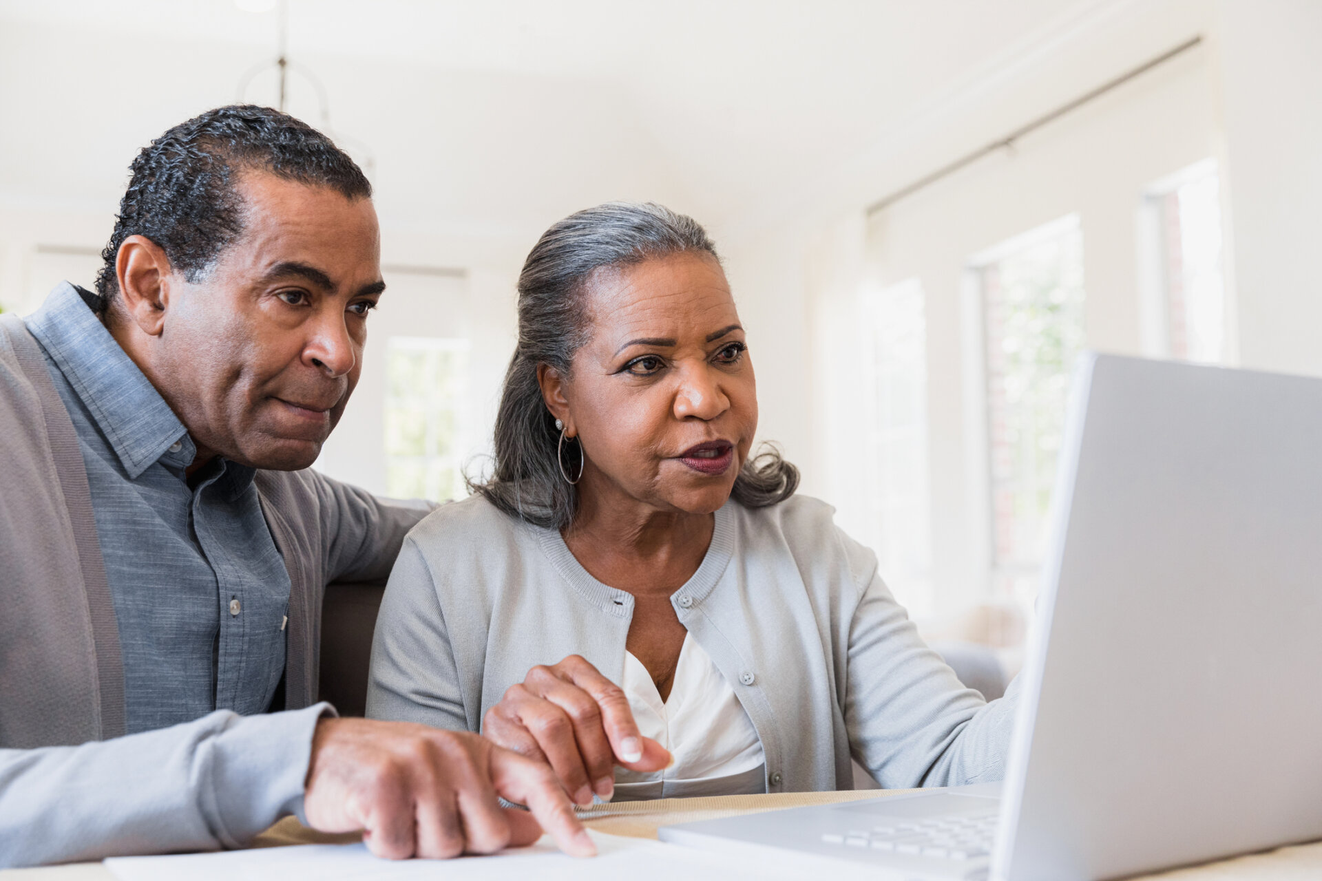 Senior man and woman sitting at their kitchen table looking at Traditions of Saginaw community information on a laptop