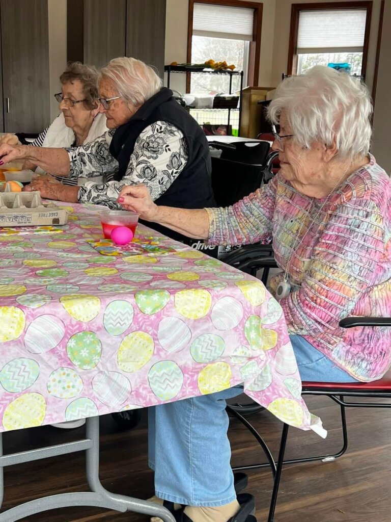 Three residents gather around a festively decorated table to dye Easter eggs together at Saginaw.
